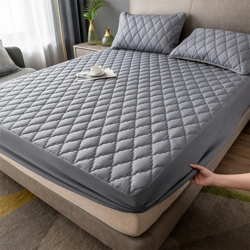 Protector gris puesto en una cama doble, una mano estira la esquina